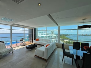Uma sala de estar espaçosa com uma varanda grande, móveis brancos e vista para a cidade.