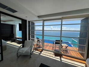 Ein modernes Zimmer mit großem Fenster mit Blick auf einen Pool und den Ozean, einem weißen Sofa und einem an der Wand befestigten Fernseher.