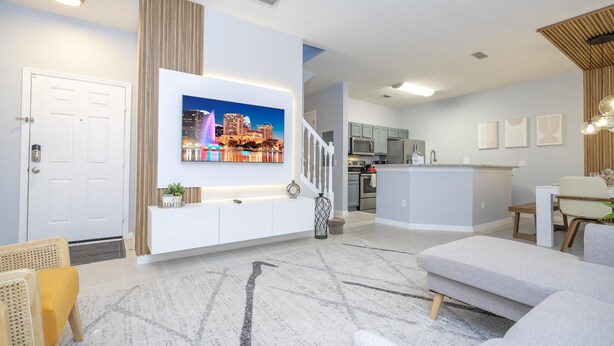 A modern living room with a flat-screen TV mounted on the wall, a staircase leading to the kitchen, and a dining area with a table and chairs. - 3012- Great Family Home near Disney (private pool) (Kissimmee)