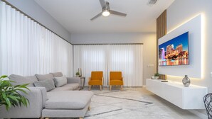 A modern living room with a sectional sofa, two armchairs, a flat-screen TV mounted on the wall, and a ceiling fan. - 3012- Great Family Home near Disney (private pool) (Kissimmee)