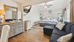 Ein Schlafzimmer mit Bett, Deckenventilator, Kommode, Stuhl und Sofa.