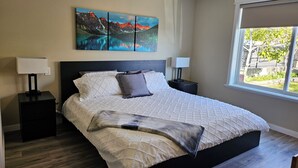 A bedroom with a large bed, two bedside tables, a window with a view, and a painting on the wall. - A Walk to the Harborfront  (Nanaimo)