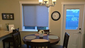 A dining area with a round table, four chairs, a chandelier, a clock, and a window with blinds. - A Walk to the Harborfront  (Nanaimo)