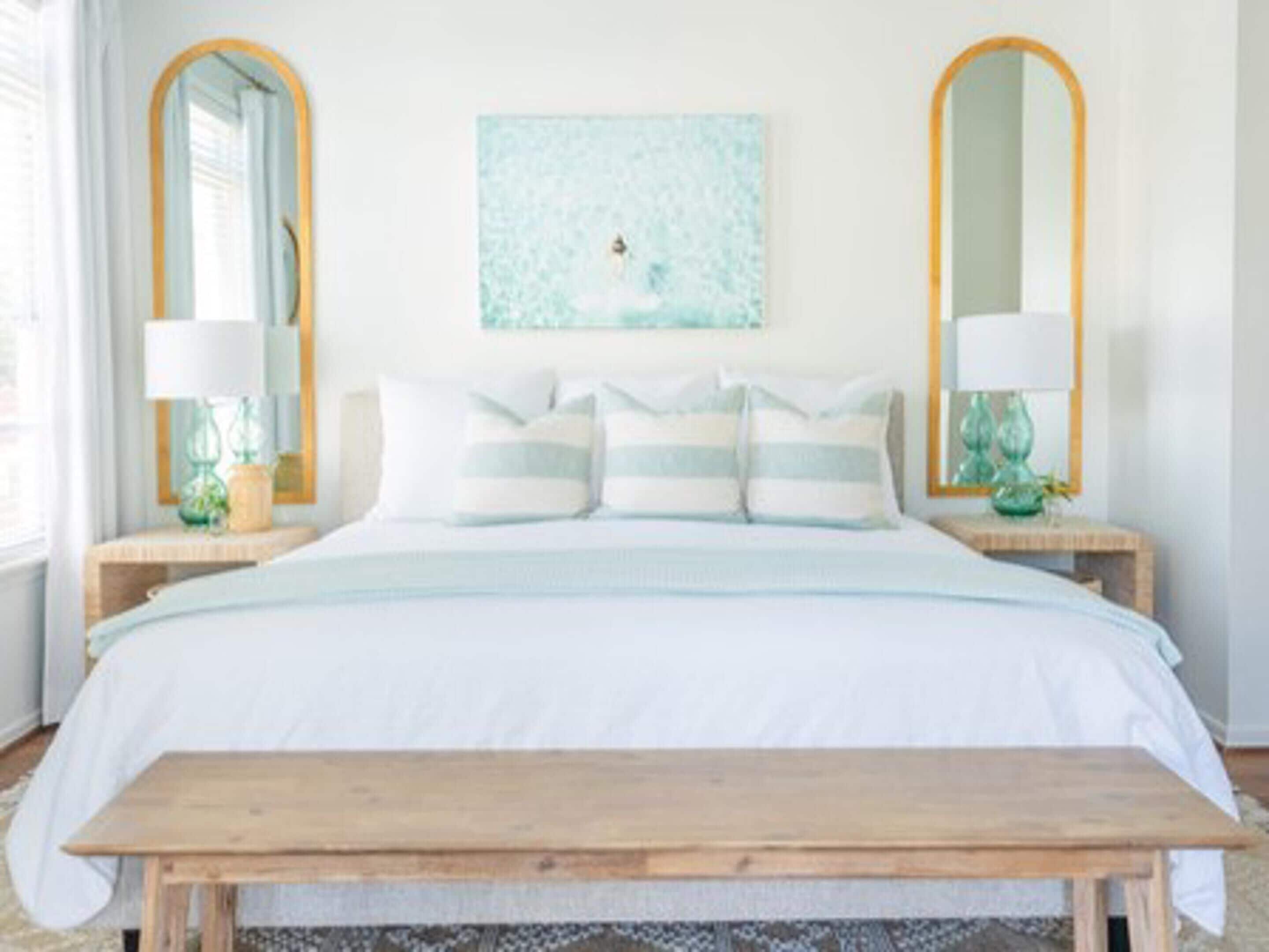 Een slaapkamer met een groot bed, twee nachtkastjes met lampen en een houten bankje.