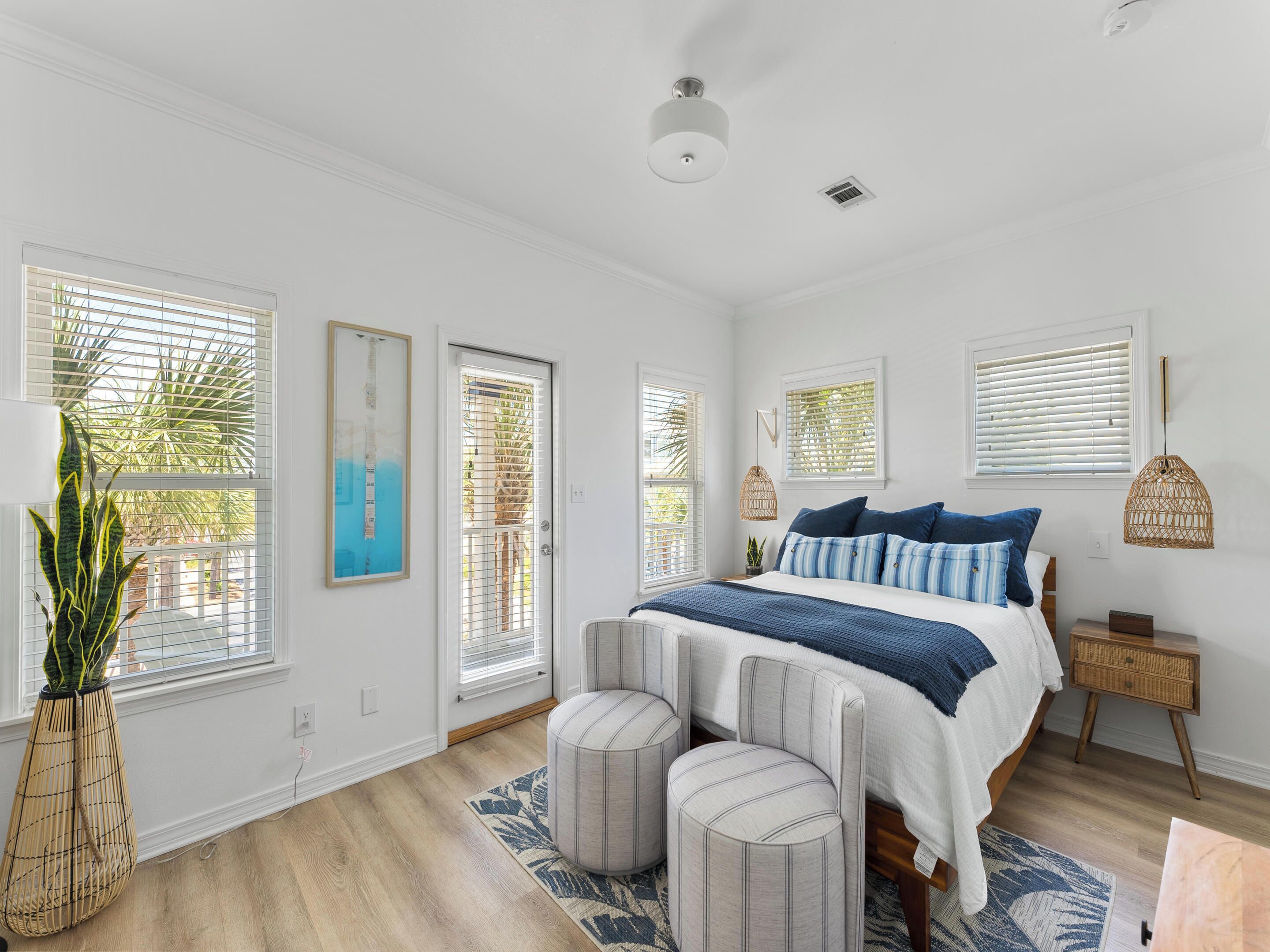 Une chambre à coucher comprenant un lit, deux tables de chevet, une commode, un luminaire suspendu et une fenêtre avec des stores.