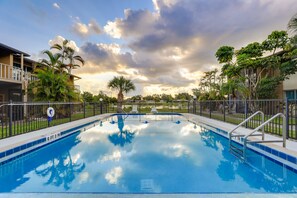 Relax by the serene pool surrounded by lush greenery and a clear sky.