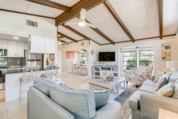 A spacious living area with a large gray sofa, a dining table with chairs, and a kitchen with white cabinets and a built-in oven. - Manasota Key Vacation Rental w/ Beach Access! (Englewood)