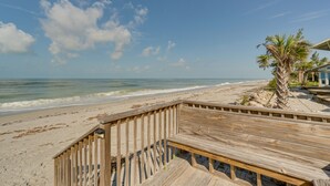 Un pontile in legno che conduce a una spiaggia, con una palma e un edificio sullo sfondo.