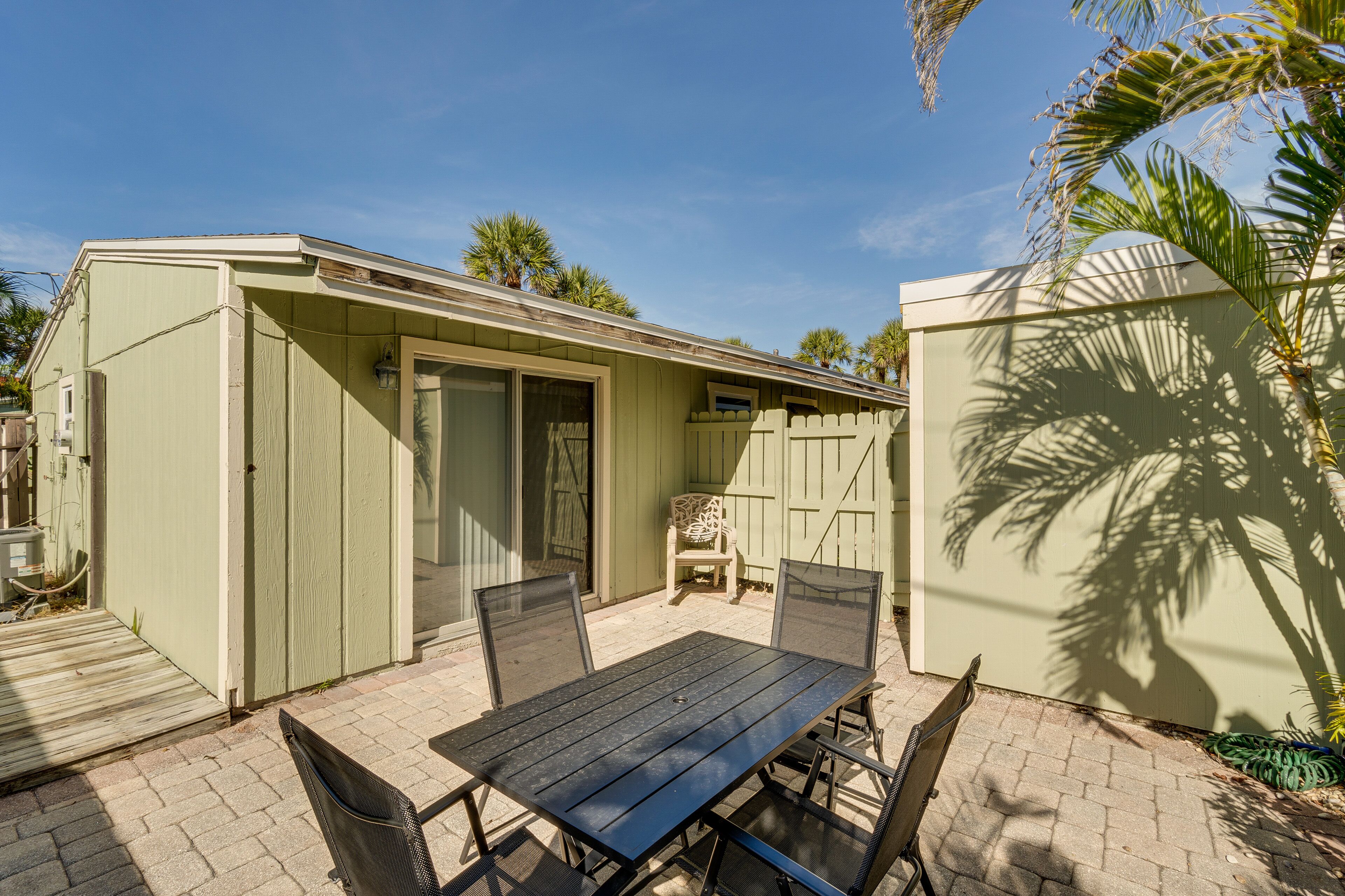 A patio with a table and chairs, a covered seating area, and a fenced yard with palm trees.