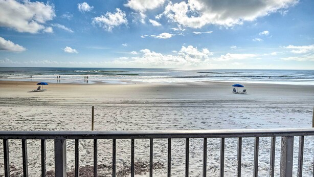 A beach with umbrellas and lounge chairs, a railing in the foreground, and a clear sky. - Daytona Beach Vacation Rental w/ Ocean Views! (Daytona Beach)