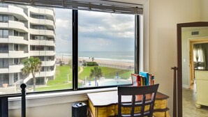 A room with a large window overlooking a pool and a building. There is a desk with a chair and a bookshelf with books. - Daytona Beach Vacation Rental w/ Ocean Views! (Daytona Beach)