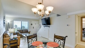 A dining area with a glass table, orange placemats, and a chandelier. - Daytona Beach Vacation Rental w/ Ocean Views! (Daytona Beach)