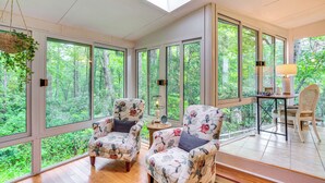A sunroom with large windows, two floral armchairs, a small table with a lamp, and a hanging plant. - 10 Mi to Sugar Mtn: ‘Bluebird Cottage’ in Newland (Newland)