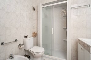 Un baño con inodoro, bidé y zona de ducha con mampara de cristal.