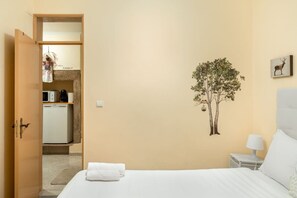 Habitación de hotel con cama, mesita de noche, lámpara, un adhesivo de árbol en la pared y una puerta que da a un rincón americano.