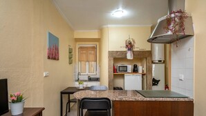 A compact kitchen with a microwave, stove, and a hanging plant. There is a dining area with a table and chairs, and a small TV on a stand. - Cozy 1-bedroom Apt|Historic location by Lisbeyond (Lisboa)