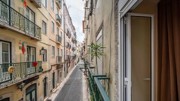 A narrow street with buildings on both sides, featuring balconies with railings and a few potted plants. - Cozy 1-bedroom Apt|Historic location by Lisbeyond (Lisboa)
