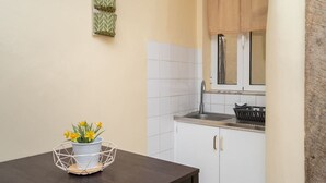 A kitchen with white cabinets, a window with beige curtains, and a table with a wireframe flower pot. - Cozy 1-bedroom Apt|Historic location by Lisbeyond (Lisboa)