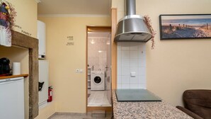 A compact kitchen with a built-in washing machine, a coffee machine, and a small seating area. - Cozy 1-bedroom Apt|Historic location by Lisbeyond (Lisboa)