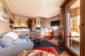 Una moderna camera d'albergo con un letto grande, un divano, un'area pranzo e vista su una casetta di legno.
