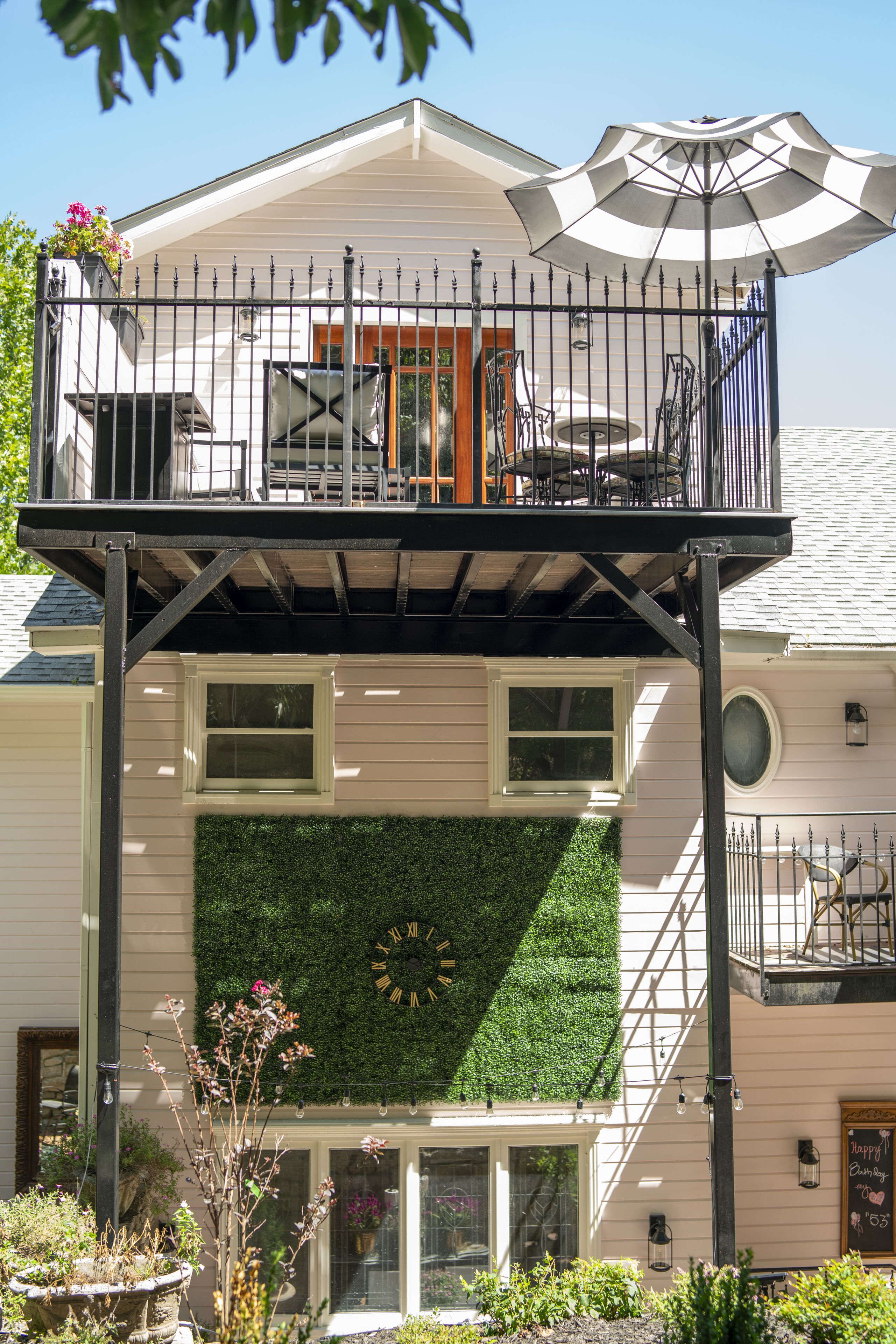 A two-story building with a balcony, a green wall, and a clock.
