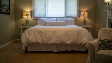 A bedroom with a large bed, two bedside tables with lamps, a chair, and a painting on the wall.