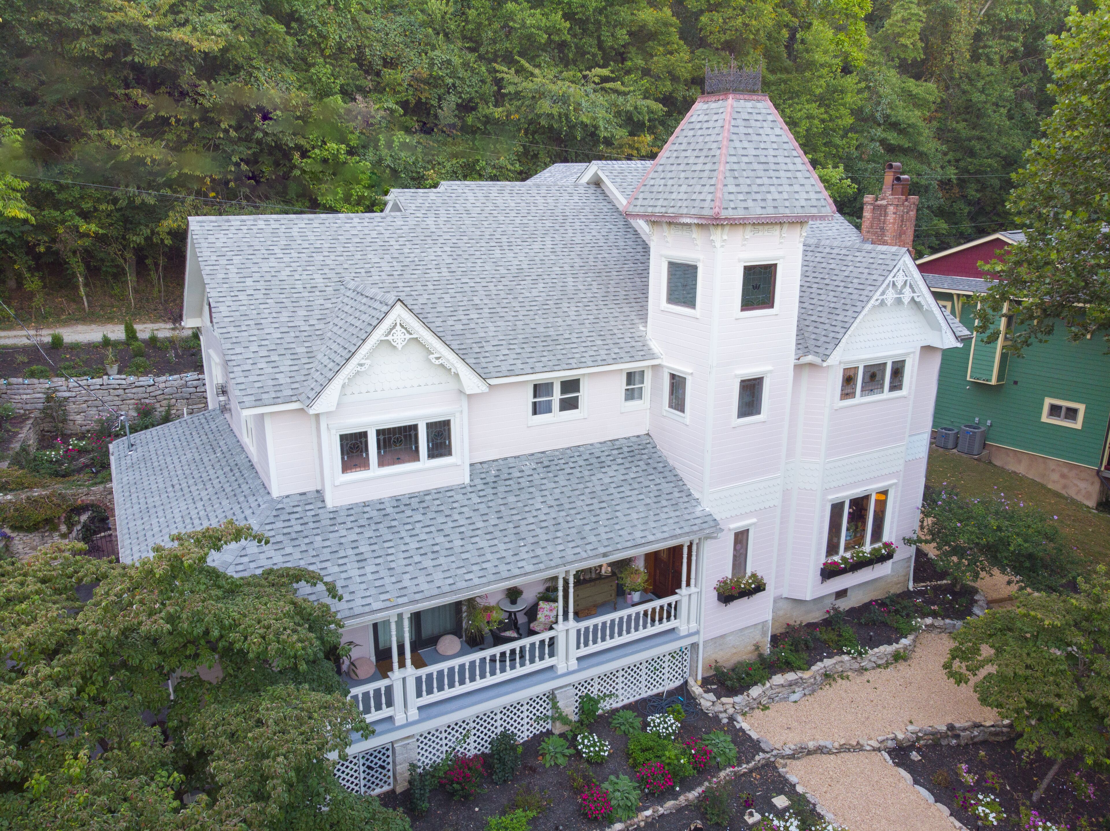 A large, two-story house with a grey roof, white exterior, and a prominent tower section.