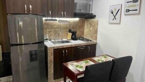 Une cuisine compacte avec des meubles en bois foncé, un réfrigérateur en acier inoxydable, un four à micro-ondes et un évier. On y trouve une table à manger avec des chaises et un petit objet décoratif accroché au mur.