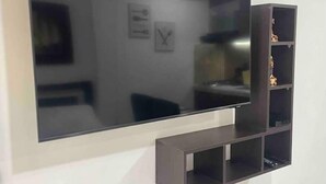 Un téléviseur à écran plat fixé au mur, avec une étagère minimaliste placée en dessous.