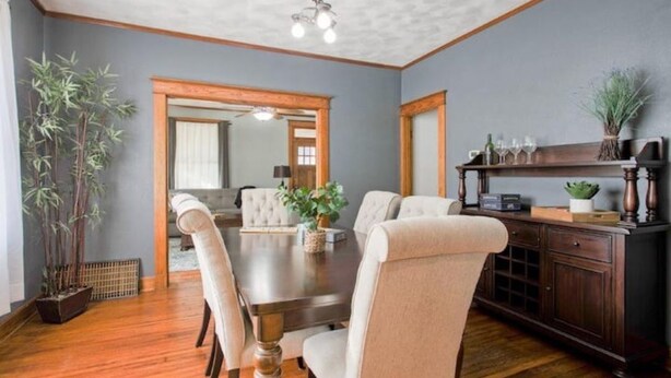 Comedor con mesa de madera, sillas tapizadas en color beige, aparador de madera oscura y una planta grande en maceta.
