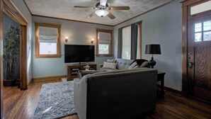 Una sala de estar con ventilador de techo, televisor de pantalla plana, sofá, lámpara y puerta de madera.