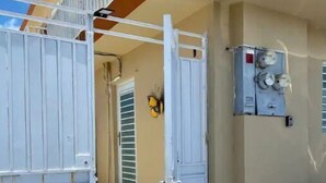 A gated entrance with a metal gate, a wall-mounted electrical box, and a door with a window. - Las Mariposas Suite Apt. 1 (Carolina)