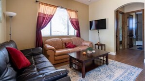 A living room with a brown leather sofa, a black leather sofa, a wooden coffee table, and a TV on the wall.