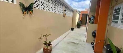 A narrow outdoor corridor with a beige wall, decorative butterfly, and potted plants.