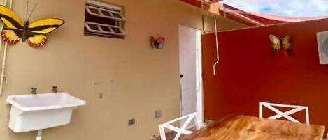 A dining area with a wooden table and white chairs, a red canopy, a wall-mounted sink, and butterfly decorations.