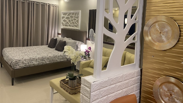 Une chambre moderne avec un grand lit, une table de chevet avec une lampe, un mur décoratif représentant des arbres et une vue sur l’intérieur de la pièce.