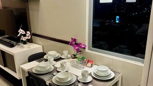 Un coin repas avec une table dressée pour quatre personnes, des chaises, une petite orchidée en pot et une fenêtre donnant sur la ville, avec une vue nocturne.