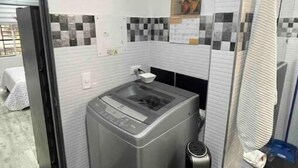 A compact laundry room with a front-loading washing machine, a dryer, and a wall-mounted ironing board. - Pretty & Modern Private Studio 202 (Cali)