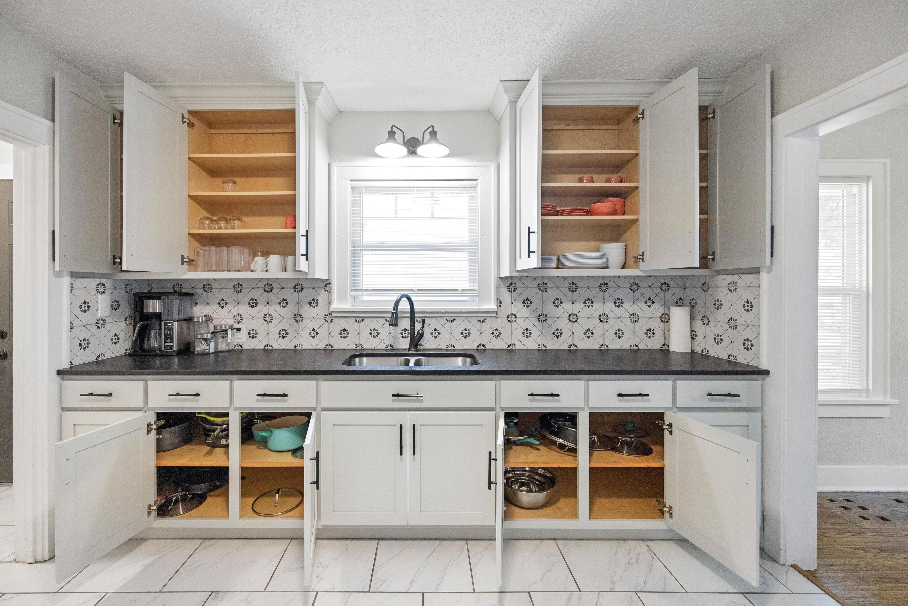 A kitchen with white cabinets, a black countertop, and a tiled backsplash.