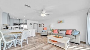 A modern living room with a grey sofa, a coffee table, and a dining area with a white table and chairs.