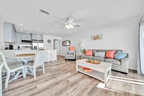 A modern living room with a grey sofa, a coffee table, and a dining area with a white table and chairs.