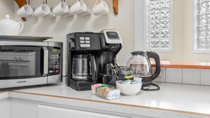 A kitchen with a microwave, coffee maker, kettle, and coffee cups on the counter.