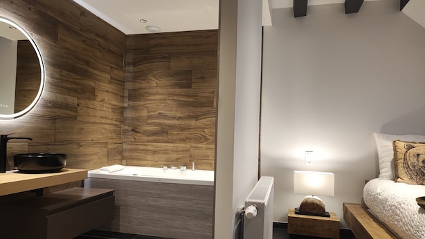 A modern bathroom with a wooden wall, a round mirror, a black basin, a white sink, and a bathtub.