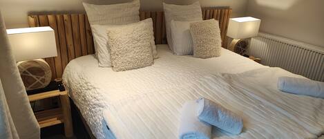 A neatly made bed with white linens and fluffy pillows, a bedside table with a lamp, and a wooden headboard.
