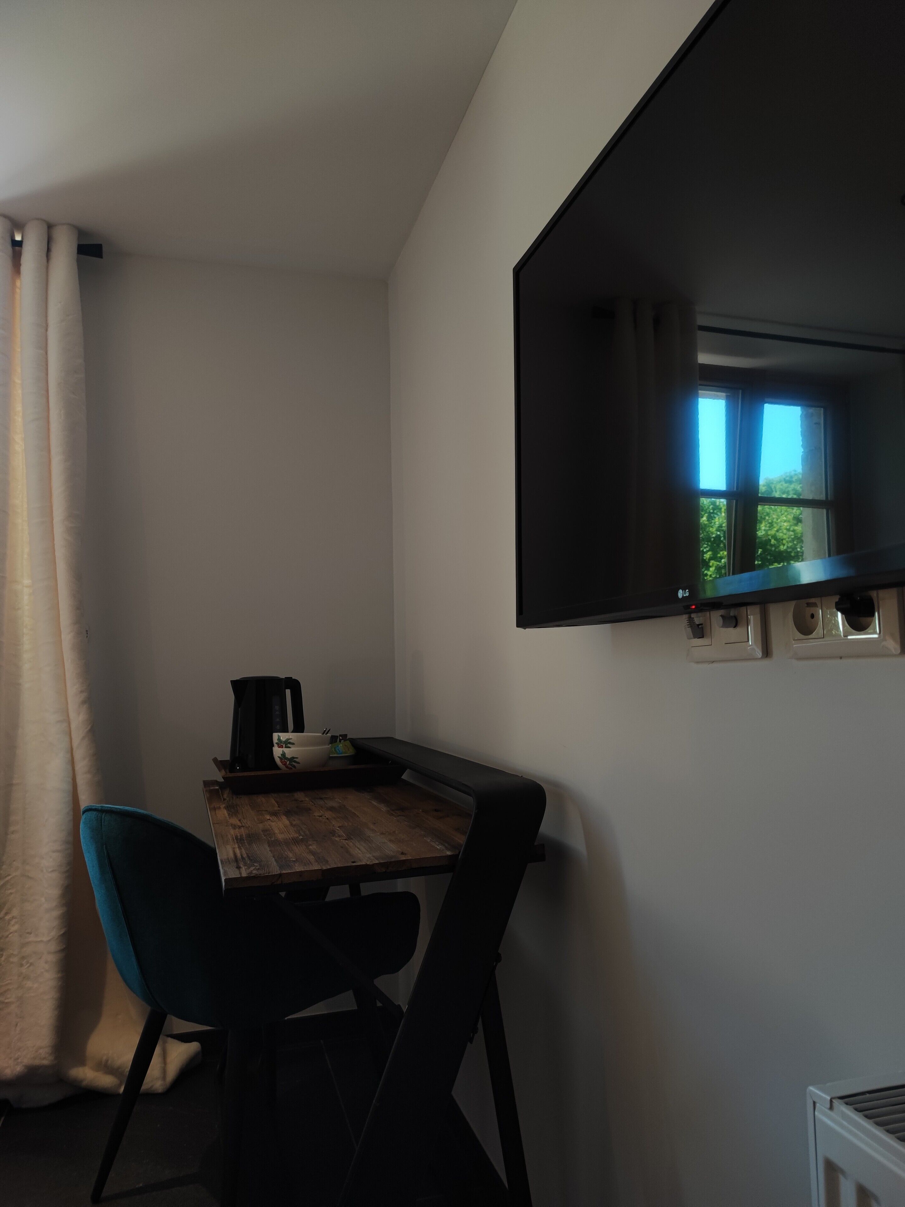 Een kleine, zwak verlichte kamer met een houten tafel, twee stoelen, een zwarte koffiezetapparaat en een raam met uitzicht op bomen.