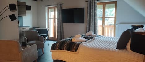 A modern bedroom with a large bed, a desk, a chair, and a TV.