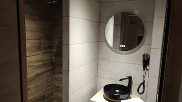 A modern bathroom with a wooden shower enclosure, a round mirror, and a black sink with a faucet.