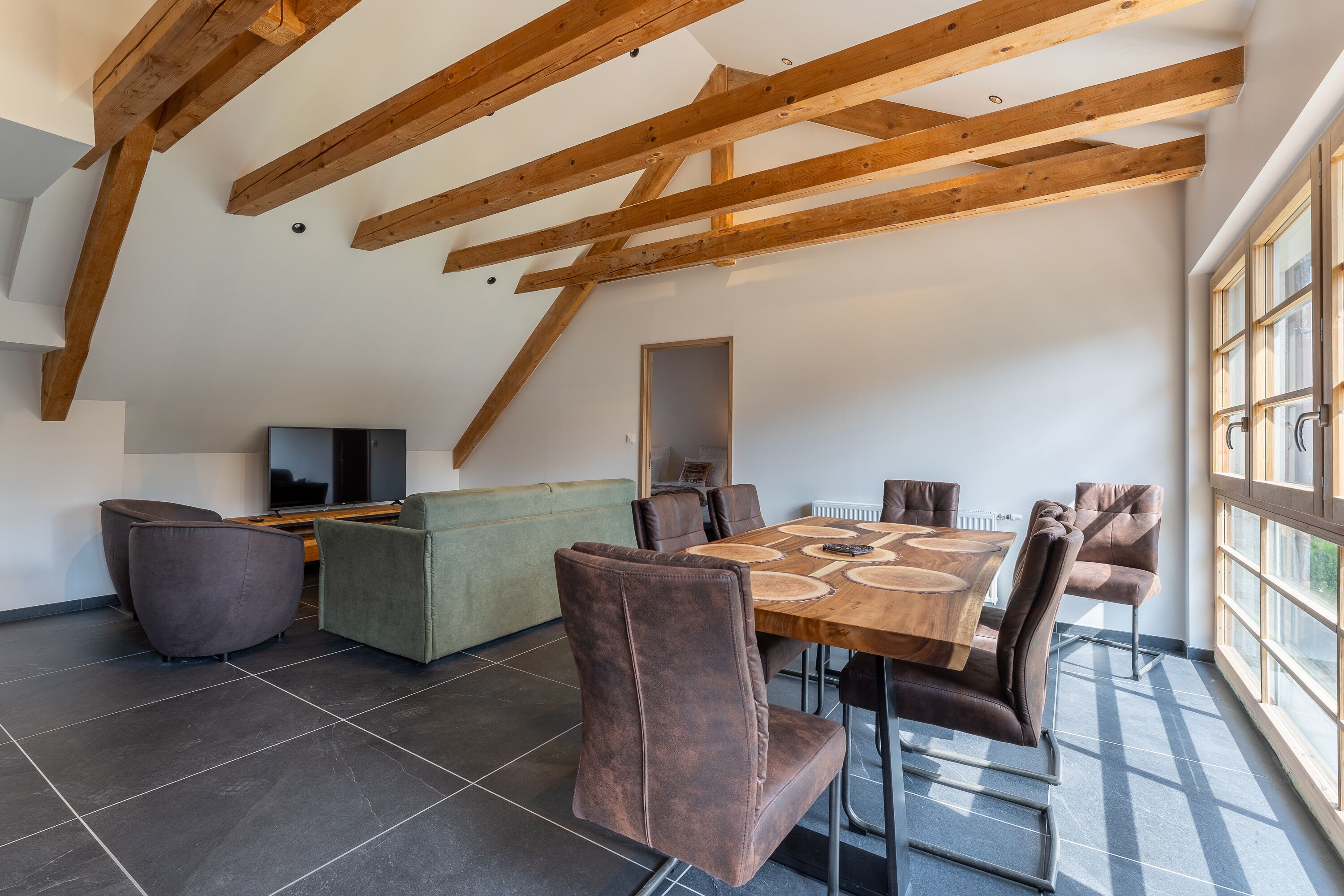 A dining area with a wooden table and chairs, a sofa, and a television.