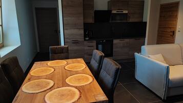 Une cuisine moderne avec des meubles de couleur sombre en bois, un four encastré et un coin repas comprenant une table en bois et des chaises en cuir.