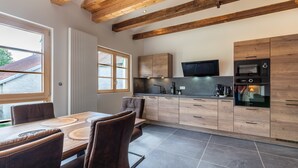 A modern kitchen with wooden beams, a dining area with a table and chairs, and a TV mounted above the counter.